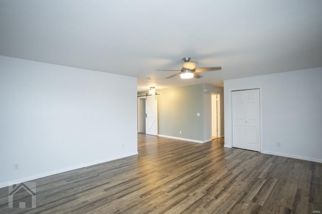 empty room with a barn door, ceiling fan, and dark hardwood / wood-style floors