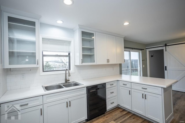 kitchen with kitchen peninsula, sink, a barn door, black dishwasher, and white cabinetry