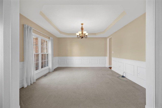 carpeted spare room featuring a notable chandelier and a raised ceiling