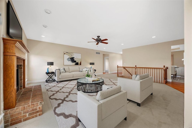 carpeted living room featuring a brick fireplace and ceiling fan