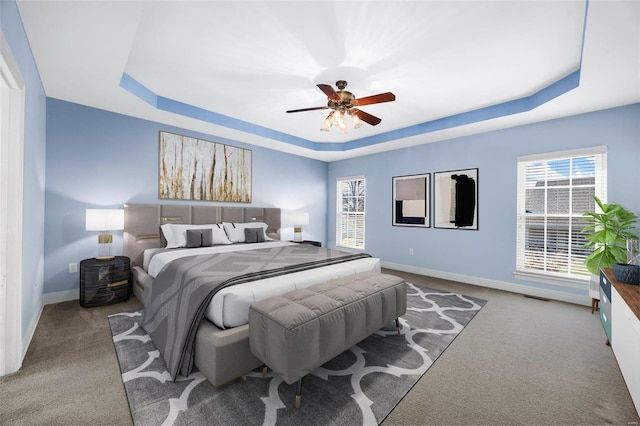 carpeted bedroom with a raised ceiling and ceiling fan