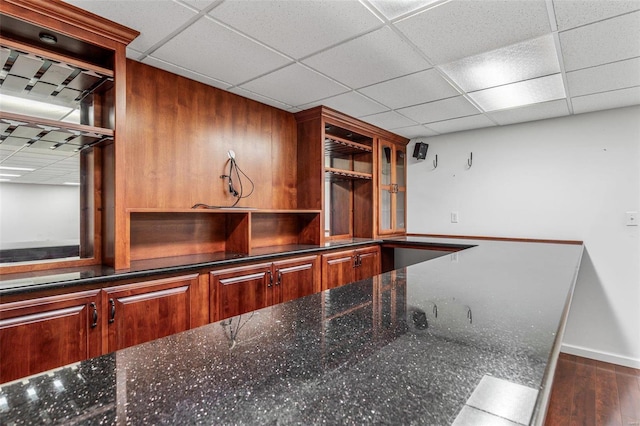 bar with dark stone countertops, a paneled ceiling, and dark hardwood / wood-style floors