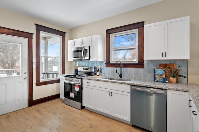 kitchen featuring sink, light wood-type flooring, light stone counters, white cabinetry, and stainless steel appliances