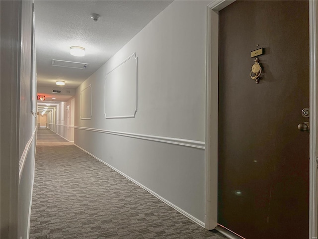 hallway featuring dark colored carpet and a textured ceiling