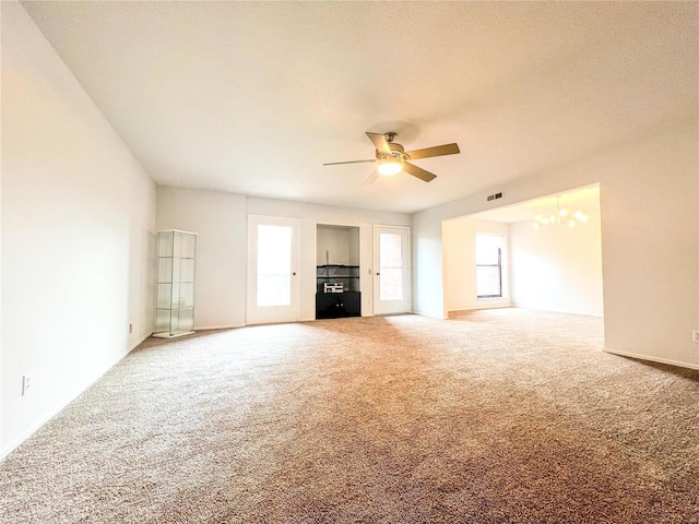 unfurnished living room featuring carpet, ceiling fan with notable chandelier, a healthy amount of sunlight, and a textured ceiling