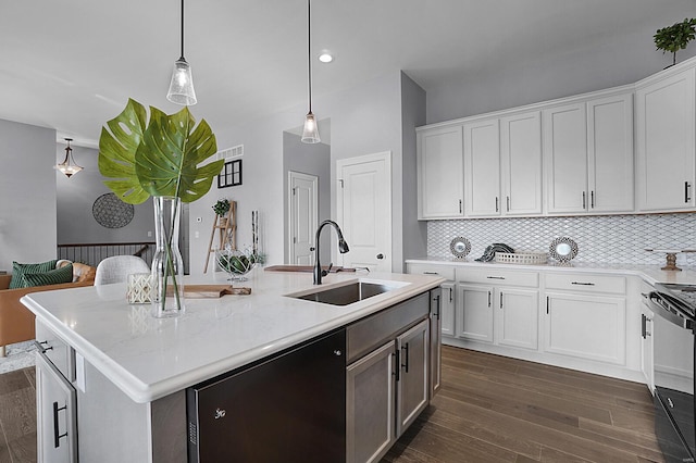 kitchen with light stone counters, sink, white cabinets, hanging light fixtures, and an island with sink