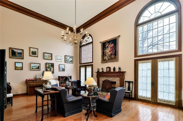 living area featuring a high ceiling, french doors, a fireplace, a notable chandelier, and light hardwood / wood-style floors