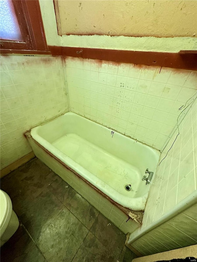 bathroom with tile patterned flooring, toilet, a tub, and tile walls