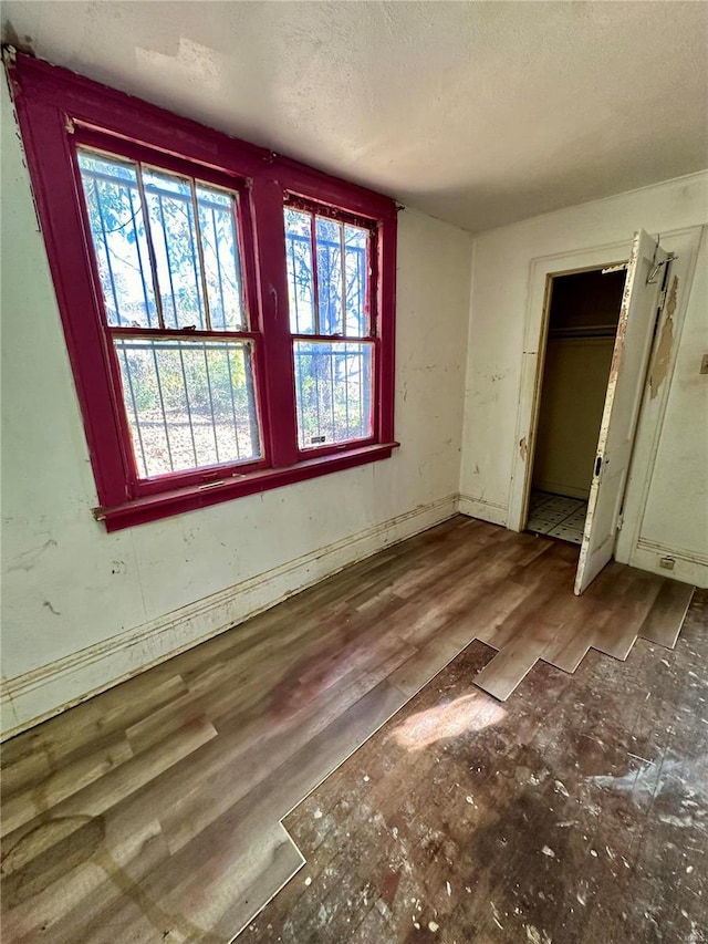 unfurnished bedroom with hardwood / wood-style flooring, a closet, a textured ceiling, and multiple windows