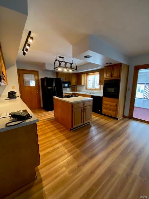 kitchen with sink, rail lighting, light hardwood / wood-style floors, a kitchen island, and black appliances