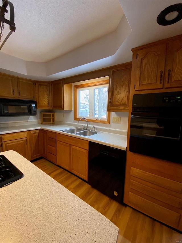 kitchen with sink, light hardwood / wood-style floors, a raised ceiling, and black appliances