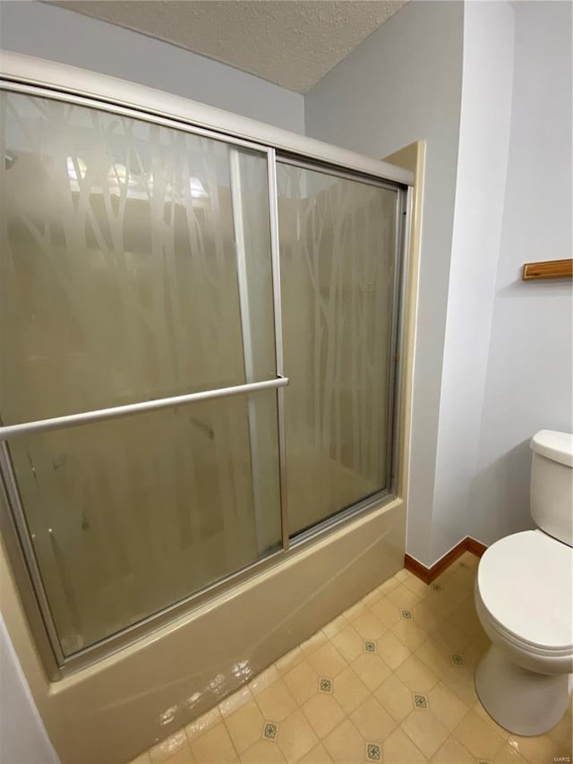 bathroom featuring tile patterned flooring, bath / shower combo with glass door, a textured ceiling, and toilet