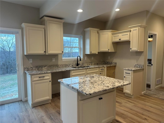 kitchen featuring light stone countertops, sink, a center island, and light hardwood / wood-style flooring