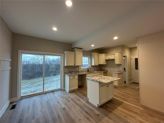 kitchen with white cabinetry, a center island, sink, and light wood-type flooring