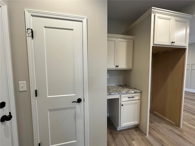 kitchen with light hardwood / wood-style floors, light stone countertops, built in desk, and white cabinetry