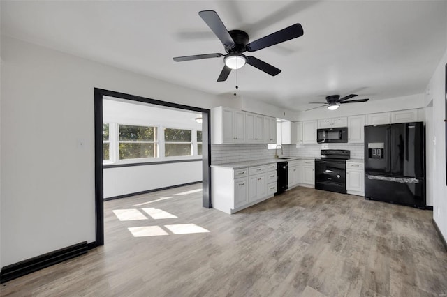 kitchen with white cabinets, decorative backsplash, light wood-type flooring, and black appliances