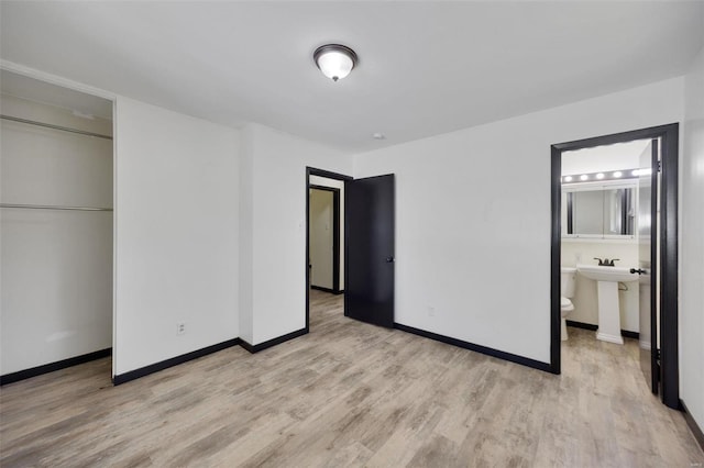 unfurnished bedroom featuring ensuite bathroom, a closet, and light wood-type flooring