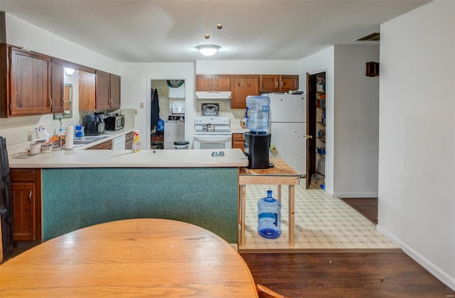 kitchen featuring dark hardwood / wood-style flooring, kitchen peninsula, washer / clothes dryer, a textured ceiling, and white appliances