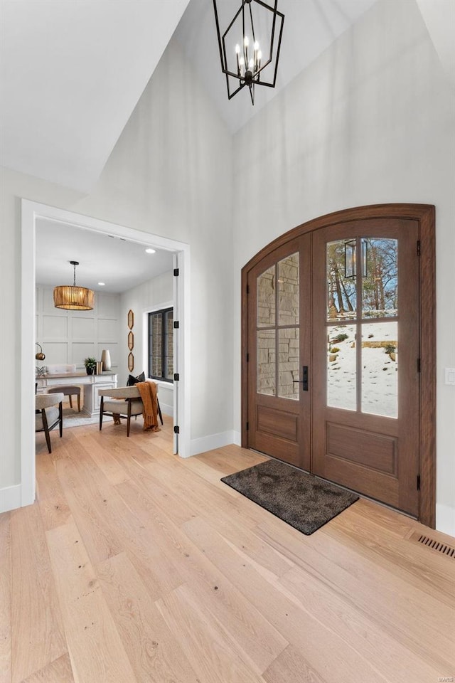 foyer entrance featuring wood-type flooring, a notable chandelier, high vaulted ceiling, and french doors