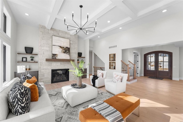 living room featuring beam ceiling, french doors, a chandelier, and light wood-type flooring