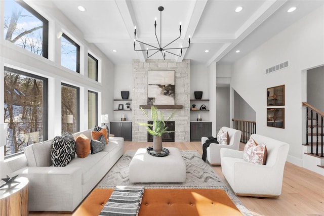 living room with beamed ceiling, a stone fireplace, built in features, and light wood-type flooring