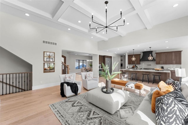 living room with coffered ceiling, beam ceiling, a chandelier, and light wood-type flooring