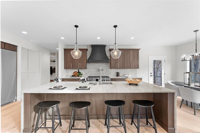 kitchen featuring custom range hood, a large island with sink, and a breakfast bar