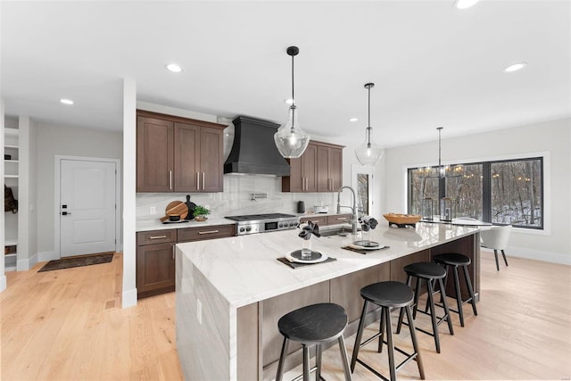 kitchen featuring sink, custom range hood, a center island with sink, and decorative light fixtures