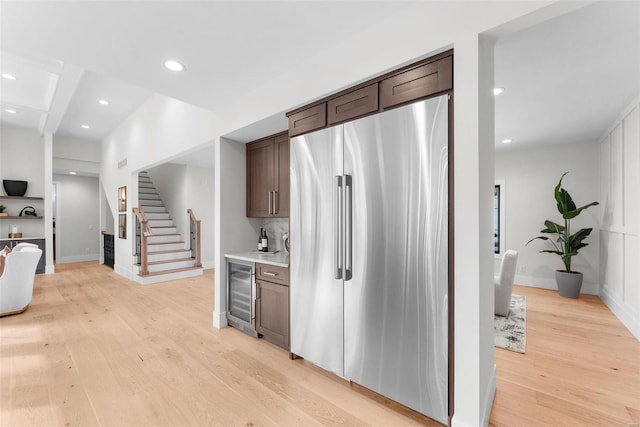 kitchen with dark brown cabinetry, light wood-type flooring, stainless steel fridge, and beverage cooler