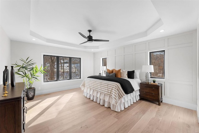 bedroom featuring a raised ceiling, light wood-type flooring, and ceiling fan