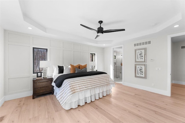 bedroom featuring ceiling fan, ensuite bathroom, a raised ceiling, and light hardwood / wood-style flooring