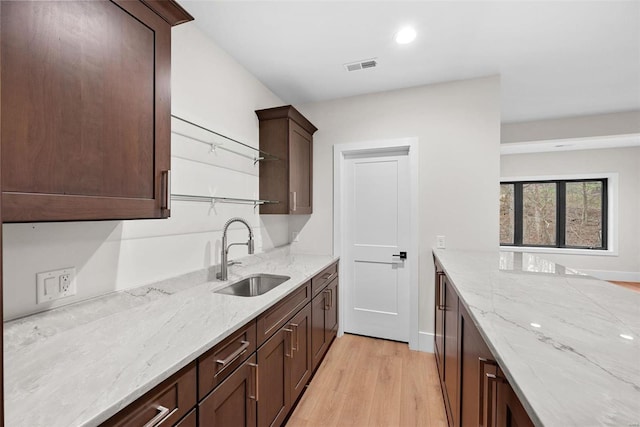 kitchen featuring light stone countertops, sink, dark brown cabinets, and light hardwood / wood-style flooring