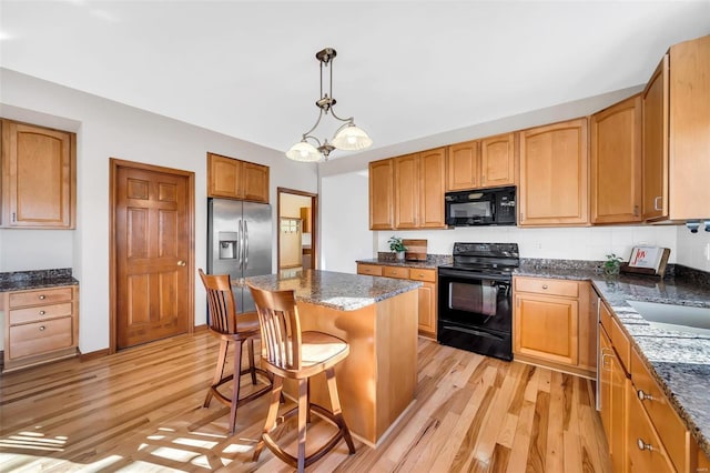 kitchen with a kitchen breakfast bar, black appliances, pendant lighting, light hardwood / wood-style floors, and a kitchen island