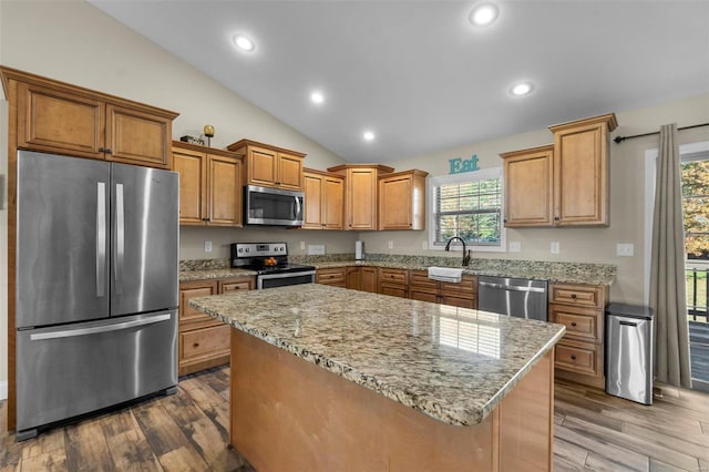 kitchen with hardwood / wood-style floors, lofted ceiling, sink, appliances with stainless steel finishes, and a kitchen island