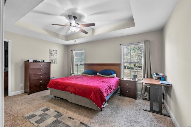 carpeted bedroom with a tray ceiling, multiple windows, and ceiling fan