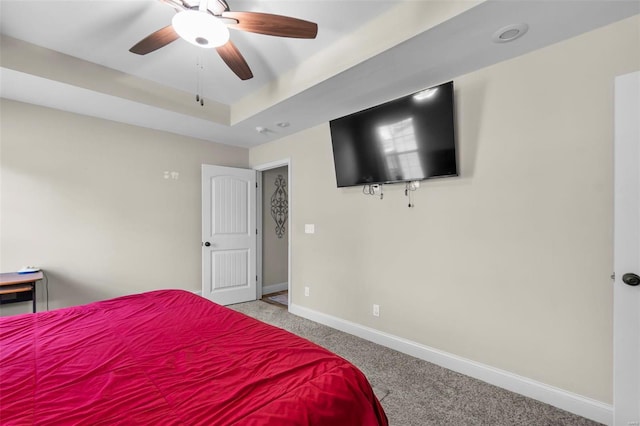 carpeted bedroom with a raised ceiling and ceiling fan