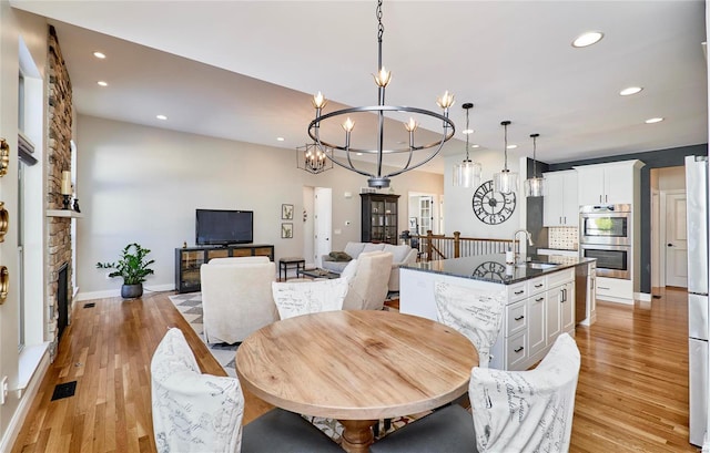 dining space featuring a fireplace, light wood-type flooring, an inviting chandelier, and sink