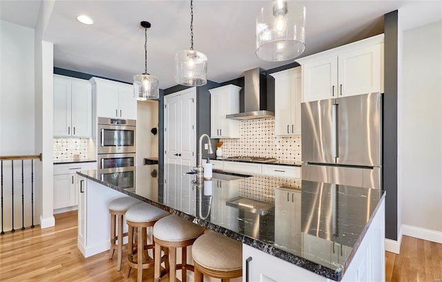 kitchen featuring appliances with stainless steel finishes, wall chimney range hood, pendant lighting, white cabinets, and a large island