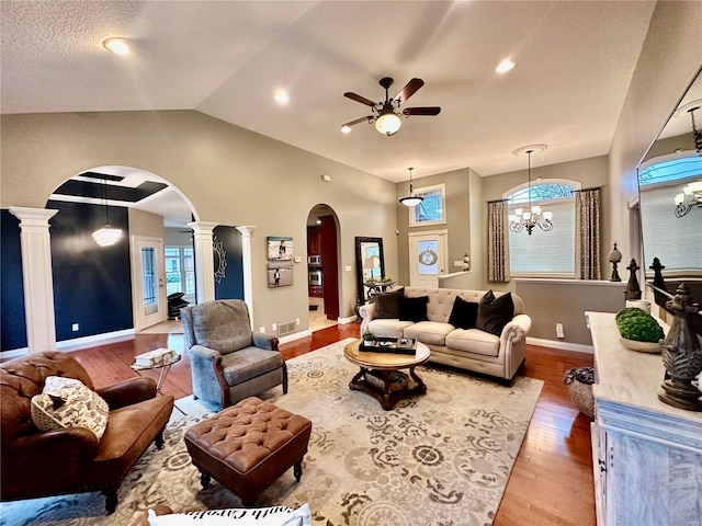 living room featuring ornate columns, ceiling fan with notable chandelier, lofted ceiling, and hardwood / wood-style flooring