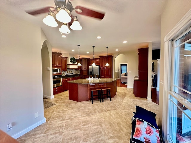 kitchen featuring dark stone countertops, ceiling fan, a center island with sink, and appliances with stainless steel finishes