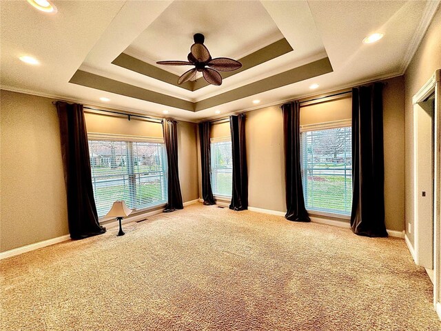 carpeted spare room featuring a tray ceiling, crown molding, and ceiling fan