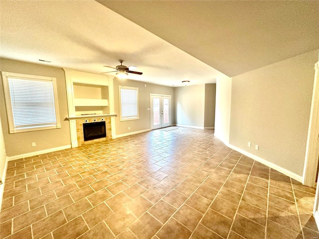 unfurnished living room featuring a tile fireplace, french doors, a textured ceiling, and ceiling fan