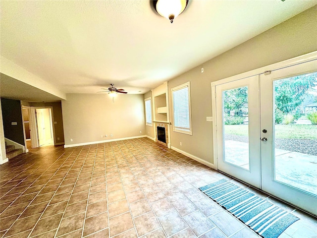 unfurnished living room featuring a tile fireplace, french doors, tile patterned flooring, ceiling fan, and a textured ceiling