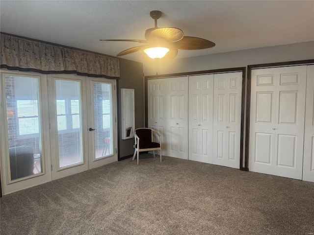 unfurnished bedroom with a textured ceiling, carpet floors, two closets, and ceiling fan