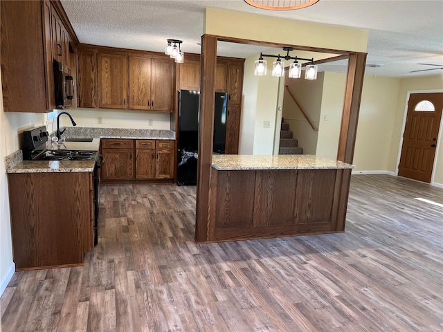 kitchen with a textured ceiling, light stone counters, black appliances, and dark hardwood / wood-style floors