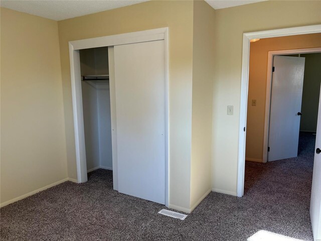 unfurnished bedroom with dark colored carpet and a closet