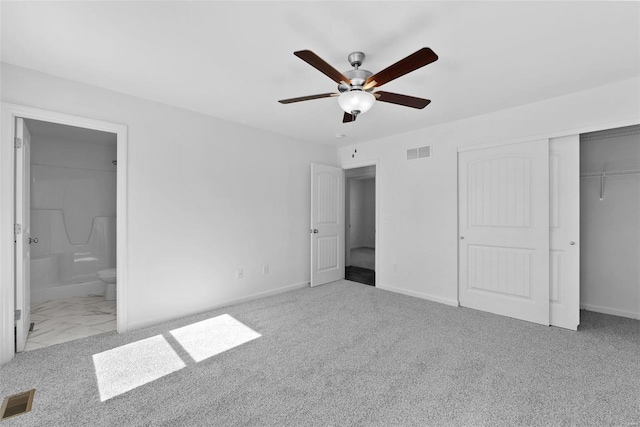 unfurnished bedroom featuring ceiling fan, a closet, light colored carpet, and ensuite bath