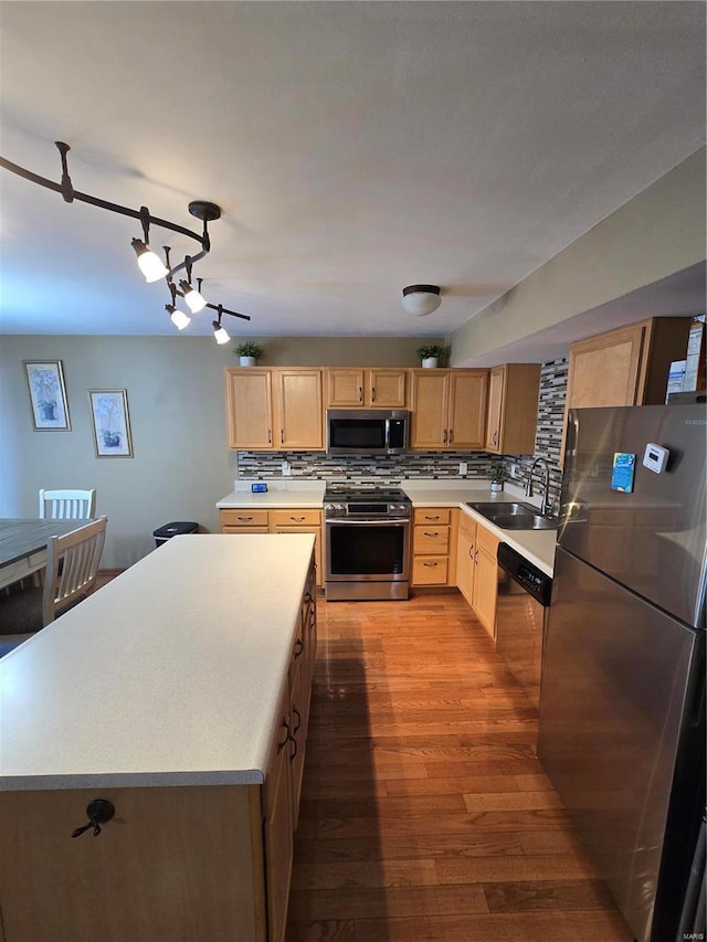 kitchen with appliances with stainless steel finishes, backsplash, wood-type flooring, a kitchen island, and sink