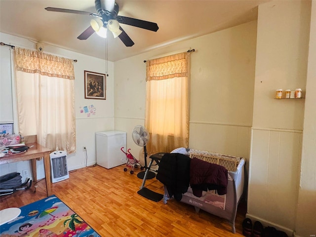 bedroom with wood-type flooring, heating unit, fridge, and ceiling fan