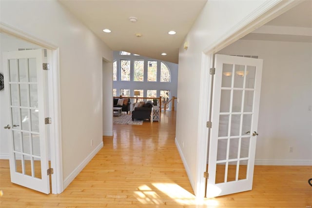 corridor with french doors, high vaulted ceiling, and light hardwood / wood-style floors